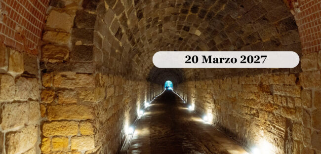 Una galleria sotterranea in pietra con volta a botte, illuminata lungo le pareti
